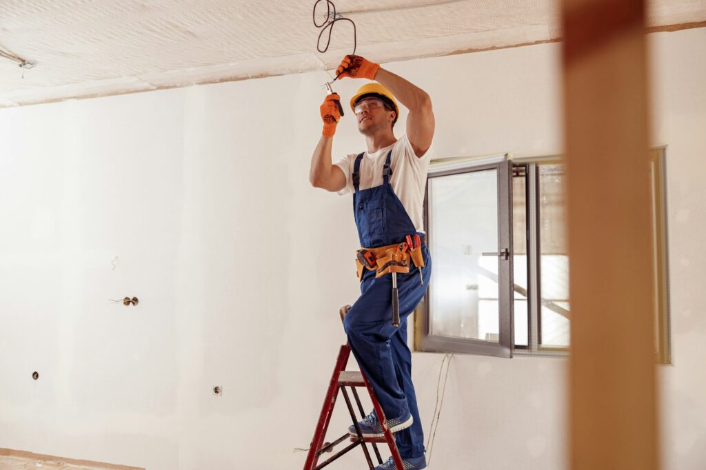 Smiling electrician fixing electric cable on ceiling